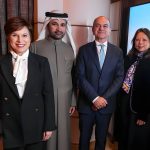 Four professionals in business attire, including a man in traditional Emirati clothing and three individuals in formal suits, standing together in an office setting for a partnership announcement
